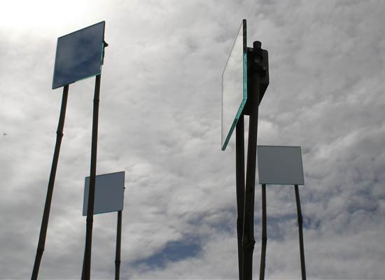 Four square mirrors mounted on pairs of bamboo canes are silhouetted against the sky. Each points in different direction, as if scanning for signals.